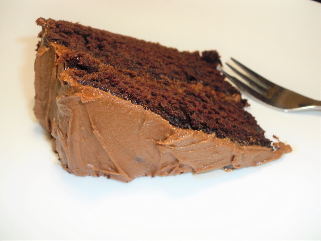A slice of dark chocolate cake with peanut butter frosting on a white plate