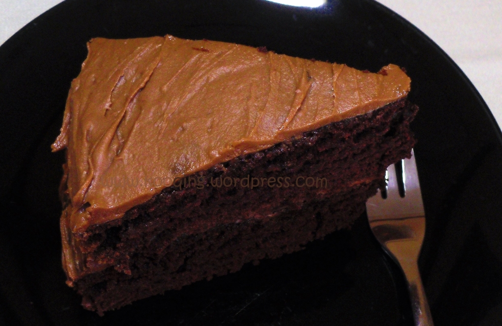 A slice of moist chocolate cake with peanut butter frosting on a black plate